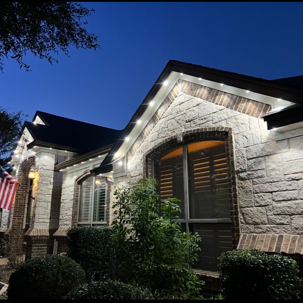 Warm white permanent roofline lighting on a stone and brick home